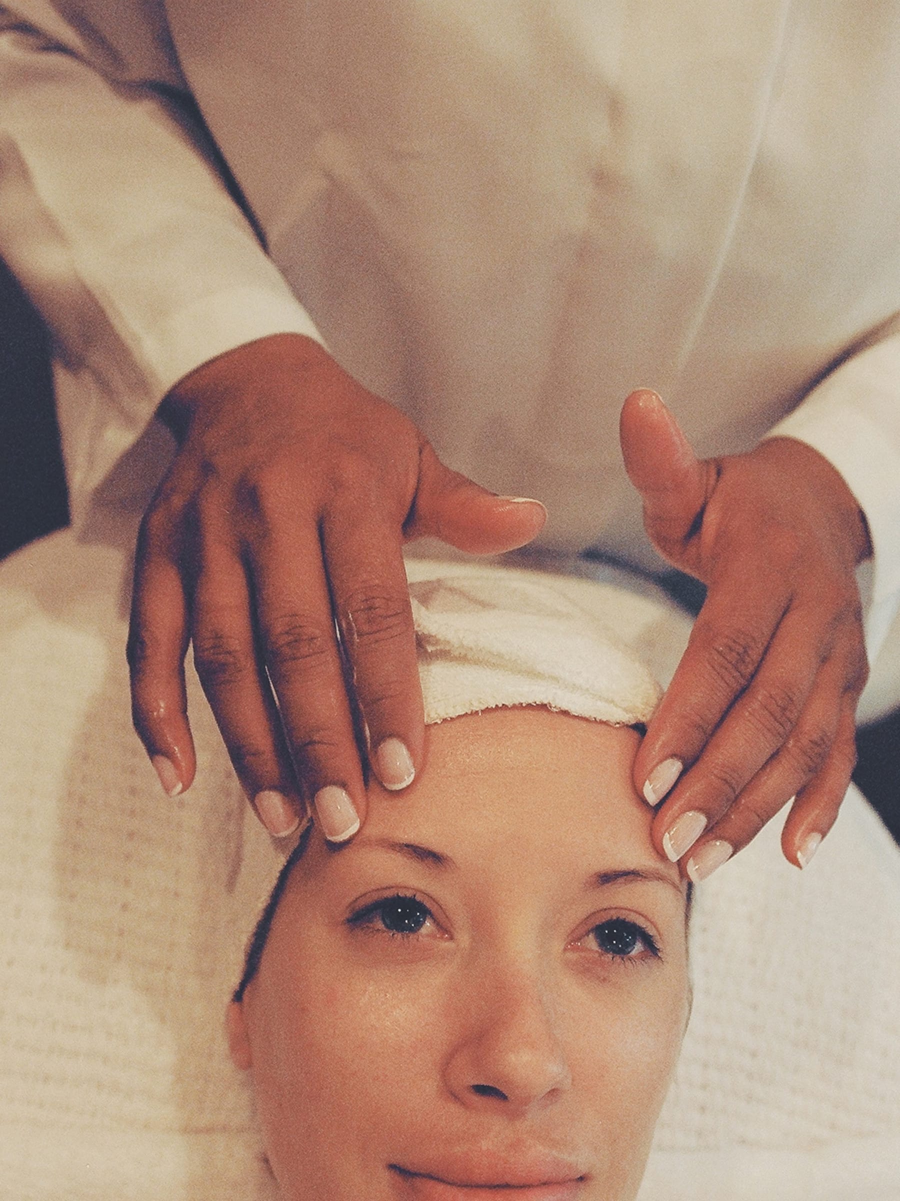 Client relaxing during a facial with a cool mask, towel wrapped around the hair